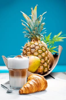 Coffee Break on a deck at the beach with a croissant and tropical fruits as a breakfast.