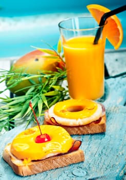 Colourful healthy tropical lunch of open ham and pineapple sandwiches topped with melted cheese accompanied by fresh mango juice