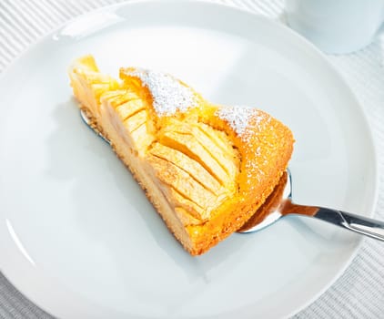 Slice of delicious golden freshly baked apple tart being served onto a white plate, high angle view