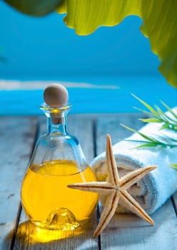 A decanter of golden aromatherapy oil , starfish and towel stand on a wooden deck above the sea in a marine spa treatment and wellness concept