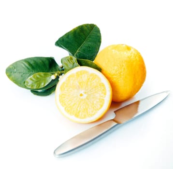 Halved and whole fresh lemons with leaves and a knife on a white studio background