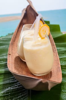 Two glasses of healthy sweet velvety banana smoothies served on a banana frond on a tropical beach