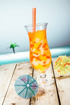 Mango Boba Cocktail Tea standing in front of a beach background with beautiful paper umbrellas.