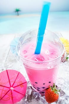 Delicious blended strawberry Bubbles Tea with berries served with a pink cocktail parasol on a deck overlooking the ocean