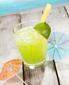 Citrus Boba Tea with bubbles and two paper cocktail umbrella in front of a swimming pool