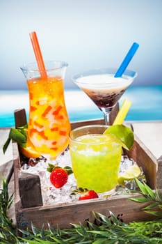 Trio of colourful tropical cocktails blended with fruit in different shaped glasses served overlooking a tropical beach