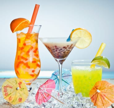 Three different boba tea cocktails with mango, orange, coffee and lime flavored. With paper umbrellas.