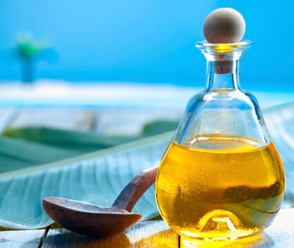 Bottle of glowing golden oil and a ladle on a deck near the sea ready for a tropical spa treatment
