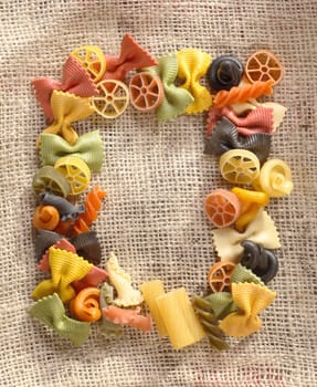 Coulorful frame on hessian material of variously shaped pastas including bowtie, wheels, and spirals.