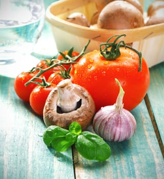 Fresh cooking ingredients for pasta including mushroom, garlic, tomato and fresh herbs on rustic wooden boards.