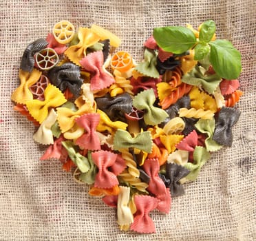 Colorful Bowtie Pasta Heart. Heart-shaped arrangement of colourfaul bowtie pastas, or farfalle, on rustic hessian material, concpetual of love and romance.