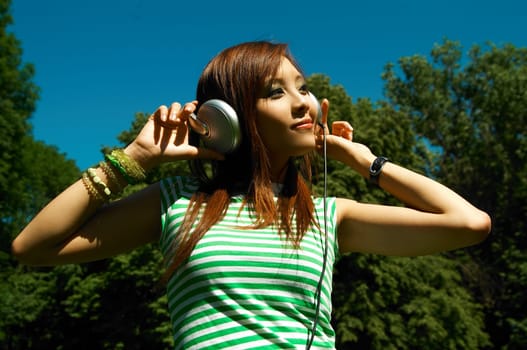 Beautiful asian young girl with headphones, listen to music on meadow