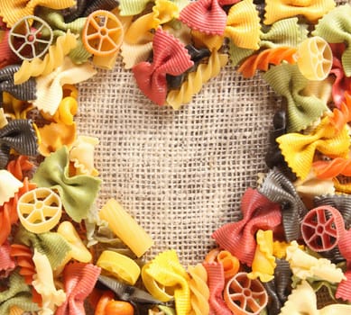 Colorful beauty Pasta Heart. Heart-shaped arrangement of colourful bowtie pastas, or farfalle, on rustic hessian material, concpetual of love and romance.