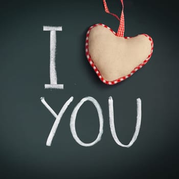 I Love You. Handwritten message on a chalkboard with a rustic needlework heart used as a symbol of love in this Valentines message.