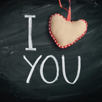 I Love You. Handwritten message on a chalkboard with a rustic needlework heart used as a symbol of love in this Valentines message.