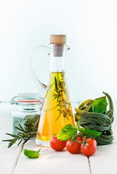 fresh tomatoes and basil with uncooked green tagliatelle and a decanter or carafe of golden olive oil on a white painted wooden background