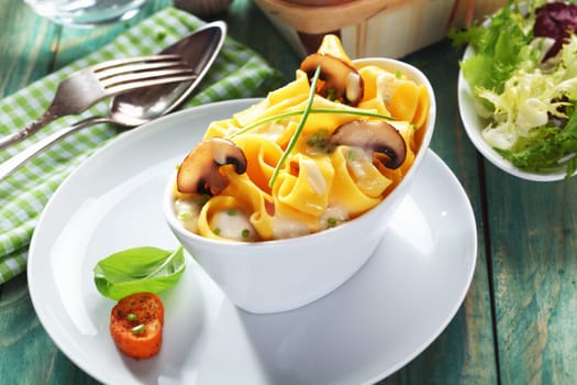 Dish of delicious mushroom tagliatelle served with salad in a rustic kitchen on green wooden boards