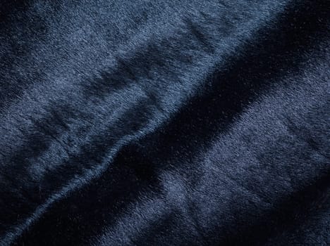 Background of a dark piece of soft supple suede leather with wrinkles