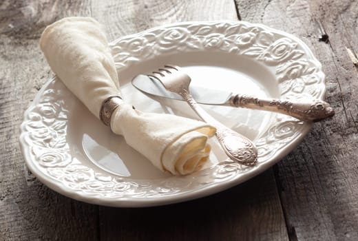 White rose patterned dinner plate with silverware and a napkin in an informal table setting