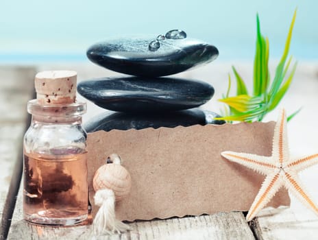 Beautiful serrated edged blank label leaning on a stack of black hot massage stones near the sea offering a gift of a marine spa treatment