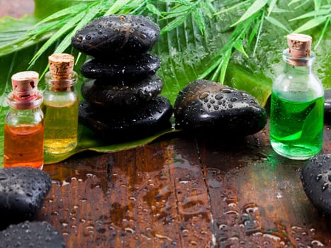 Bottles of essential oil plant extracts and smooth black massage stones in an aromatherapy spa treatment still life