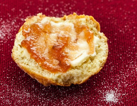 Home made scone with butter and red jam on red tablecloth