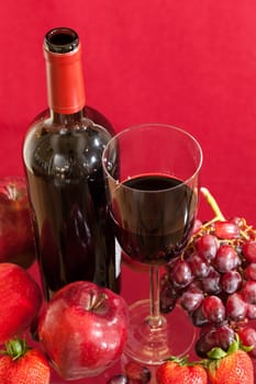 Red wine bottle and red wine in glass with red apples, grapes and strawberries