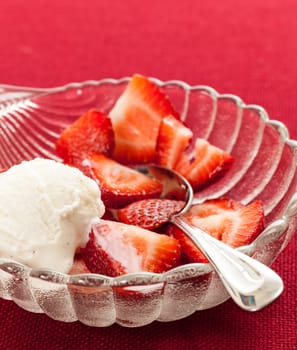 Glass dish with freshly sliced strawberry fruits against a red tablecloth with icecream