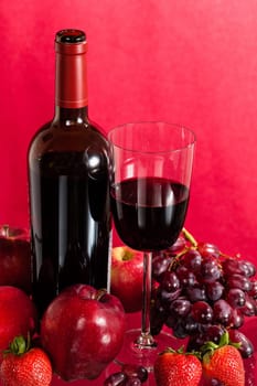 Red wine bottle and red wine in glass with red apples, grapes and strawberries