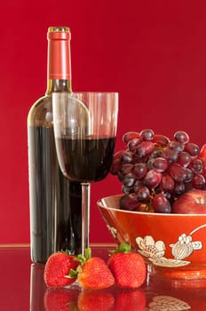 Red wine bottle and red wine in glass with red apples, grapes and strawberries