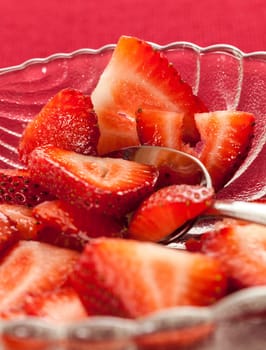 Glass dish with freshly sliced strawberry fruits against a red tablecloth
