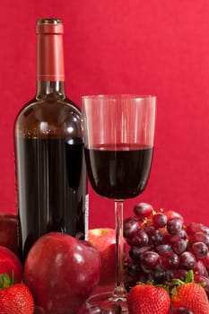 Red wine bottle and red wine in glass with red apples, grapes and strawberries