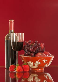 Red wine bottle and red wine in glass with red apples, grapes and strawberries