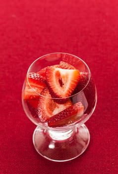 Glass dish with freshly sliced strawberry fruits against a red tablecloth