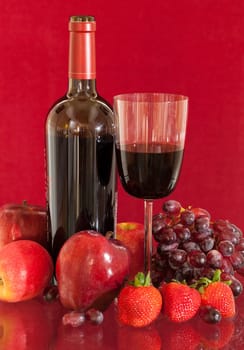 Red wine bottle and red wine in glass with red apples, grapes and strawberries