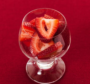 Glass dish with freshly sliced strawberry fruits against a red tablecloth