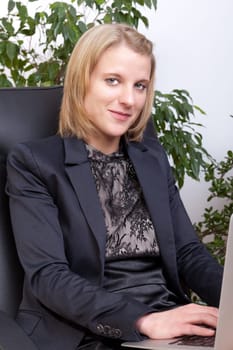 Young businesswoman with notebook on knees smiling at camera