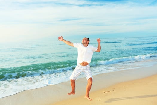 Happy man jumping on the beach at sunrise