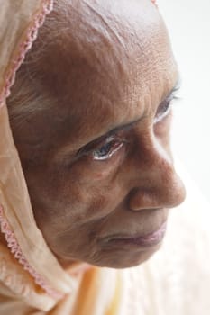 An elderly woman gazes thoughtfully while wearing a light scarf.