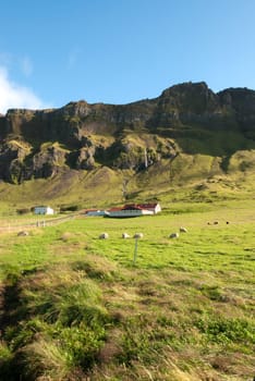 farm and waterfall in the mountains of Iceland