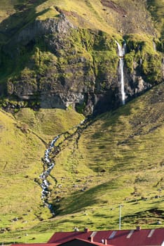 farm and waterfall in the mountains of Iceland