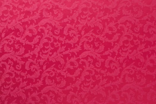 Abstract background of a heavy red brocade fabric with interwoven repeat design.