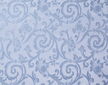 Abstract background of a heavy light blue brocade fabric with interwoven repeat design.
