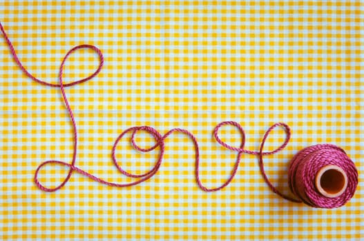 The word love drawn out with purple thread and a checked fabric background.