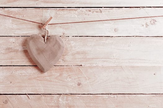 Quaint rustic wooden heart hanging from a peg against wooden boards with copyspace in a concept of love and romance