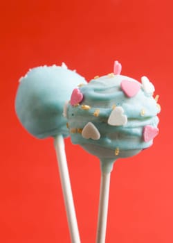 Cake pops with heart shaped candy on red background