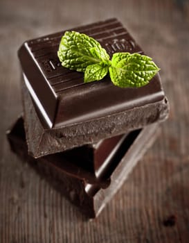 stack of chocolate pieces with a leaf of mint on wooden background