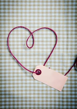 Heart drawn with purple thread through a tag over a checkered fabric pattern
