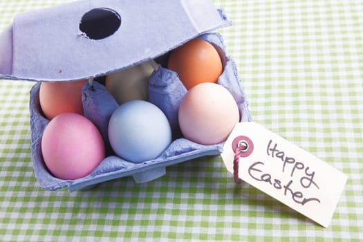 Egg carton with different colored Eggs. On a green checked background with a handwritten memo Happy Easter