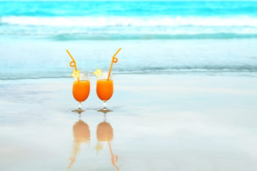 Two glasses of orange juice on tropical beach